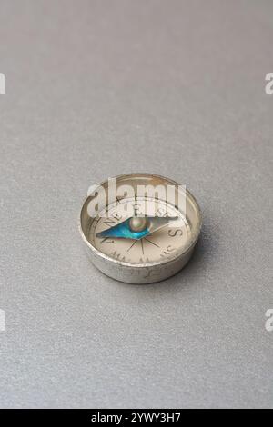 small round vintage pocket compass isolated on gray textured background, white dial with markings for cardinal directions and points towards north Stock Photo