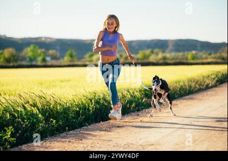 Beautiful young blonde woman running in the field with her greyhound dog. Stock Photo