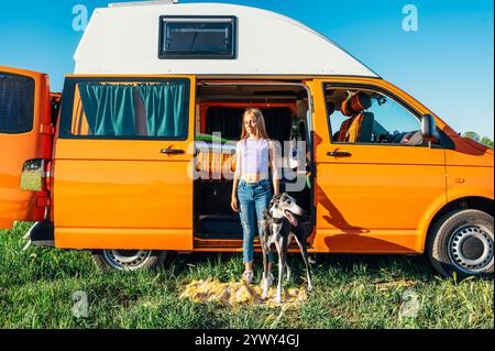 The happy girl with the dog has fun on a wonderful camping day. Van life concept. Stock Photo