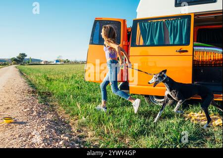 The happy girl with the dog has fun on a wonderful camping day. Van life concept. Stock Photo