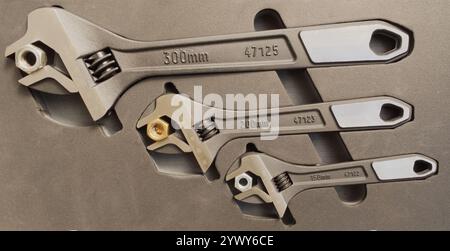 Closeup of three different sized adjustable wrenches in a fitted case, each holding a steel nut in the open jaws. Stock Photo