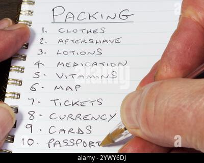 Closeup of a hand using a pen to write in a notebook a numbered packing list of items for business or leisure travel. Stock Photo