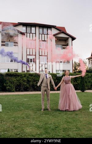 bride in lavender dress and groom on green meadow with colored smoke Stock Photo