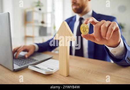 Man stock trader sitting at desk working in office with bitcoin and wooden arrow symbolizing growth Stock Photo