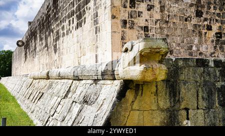 Kukulcan Serpent head sculpture close up with view of the West wall Stone Ring at the Great Ball Court,Juego de Pelota,Chichen Itza,Mexico Stock Photo