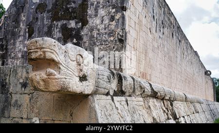 Kukulcan Serpent head sculpture close up with view of the east wall Stone Ring at the Great Ball Court,Juego de Pelota,Chichen Itza,Mexico Stock Photo