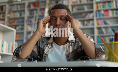 African American man guy male student massage temples headache exam tired library high school university touching head migraine eyes closed study Stock Photo
