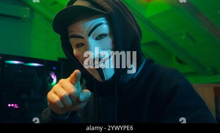 Lviv, Ukraine - June 03, 2024: Hacker anonymous typing computer looking at camera pointing finger programmer attack cyberspace fraud burglar internet Stock Photo
