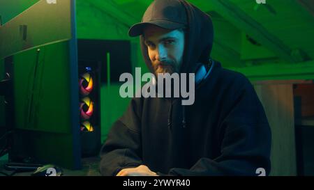 Hands typing keyboard computer Caucasian man programmer hacker looking at camera wink guy ai server system virus dangerous hooded male security Stock Photo