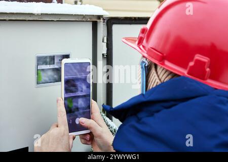 Engineer electric reads readings of electric meter using mobile device. Stock Photo