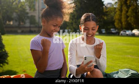 Multiracial school students pupils schoolgirls girls using mobile phone outdoors children African American little kids friends classmates gadget Stock Photo