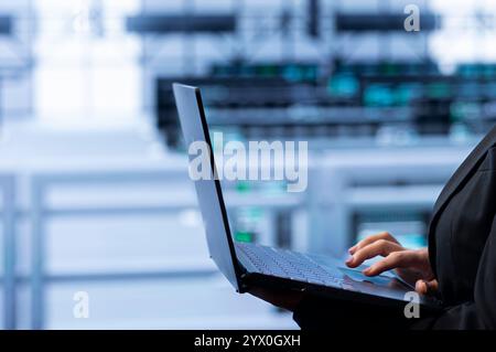 Software developer in data center making sure rackmounts are functioning optimally. Close up of specialist in server farm using laptop to monitor energy consumption across supercomputer rigs. Stock Photo