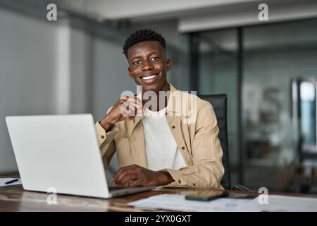Happy young African business man looking at laptop working in office. Stock Photo