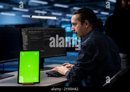 Technician in server hub using green screen tablet to repair equipment storing datasets. IT specialist using mockup device to do debugging on rigs doing computational operations Stock Photo