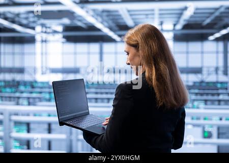 Technician in data center checking rigs and hardware, doing maintenance. IT specialist planning and executing high tech server hub facility migrations and upgrades using notebook Stock Photo