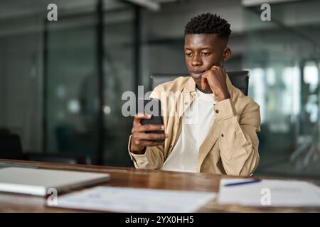 Young busy African business man sitting in office holding cellphone. Stock Photo