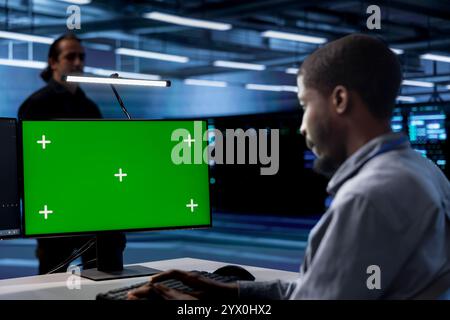 Employee using green screen PC to check for signs of imminent failure in data center supercomputers. Engineer working at chroma key PC to prevent damages in server farm, monitoring critical systems Stock Photo