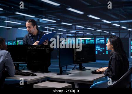Multiethnic staff members in data center updating systems, protecting equipment from damaging software vulnerabilities. Diverse team of engineers looking for bugs causing infrastructure to slow down Stock Photo