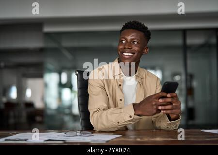 Happy African business man looking away holding phone using smartphone at work. Stock Photo