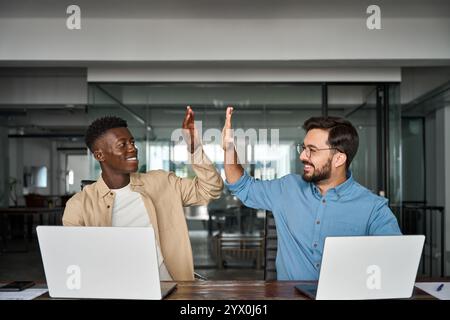 Happy diverse professional male employees team giving high five at work. Stock Photo