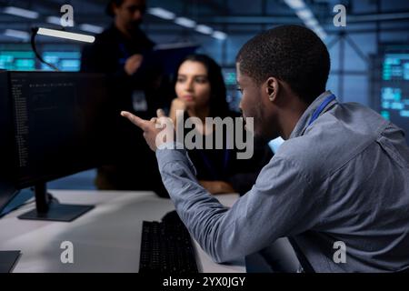 Multiethnic team reconfiguring server farm to optimize it for data processing requirements of customers. Coworkers collaborating to ensure data center equipment operates efficiently Stock Photo