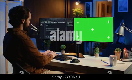 Programmer typing complex code on green screen computer in neon lit home office, developing software application. Teleworking IT specialist doing remote project tasks on mockup PC monitor, camera B Stock Photo