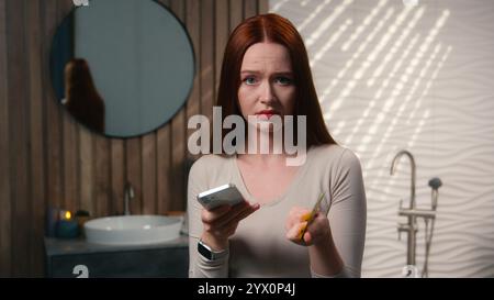 Confused upset girl Caucasian woman lady female buyer in home bathroom using cellphone money transaction wrong credit card number digital bank phone Stock Photo