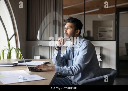 Businessman reflecting on work-related issue seated at desk with laptop Stock Photo