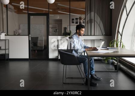 Focused Indian employee analyzing data, or writing emails on laptop Stock Photo