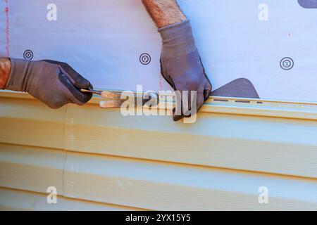 Worker carefully installs vinyl siding on house, ensuring level alignment while using hammer tools. Stock Photo
