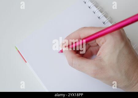 Caucasian hand writing with a pink ballpoint pen on blank page notebook. Office supplies, handwriting activity, reminder notes, content creation. Stock Photo