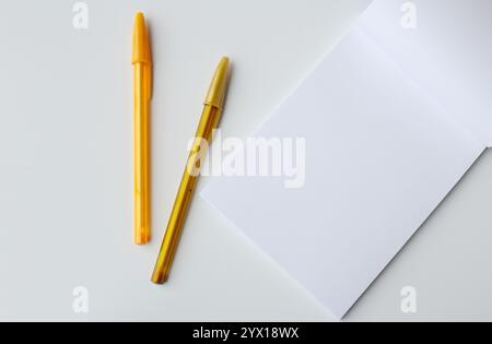 Two golden ballpoint pens on top of a blank paper notepad page. Creative stationery for back to school activities. Writing letter, drawing lesson. Stock Photo