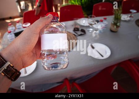 A hand holds a small bottle of spring water with a blank white label. The simple, transparent design awaits custom branding, symbolizing everyday hydr Stock Photo