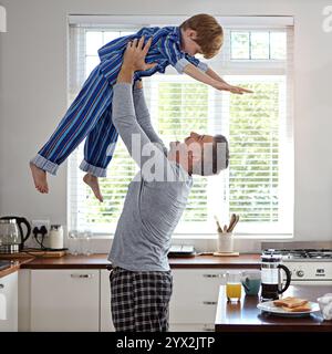 Kitchen, father and flying with boy for bonding, fun or happy in morning with pajama. Apartment, people and parent for lifting with smile for support Stock Photo