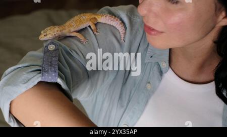 A close-up of a smiling woman interacting with a gecko on her arm. The image emphasizes companionship and the growing appreciation for reptiles as Stock Photo