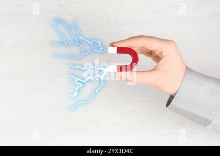 Woman holding horseshoe magnet with lightnings on light background, closeup Stock Photo
