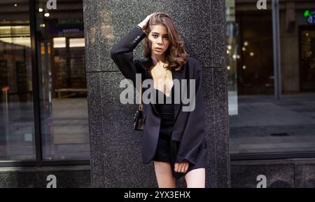Portrait Stylish young brunette woman with long hair wearing elegant outfit oversize black blazer, beautiful model stands, poses on dark gray backgrou Stock Photo