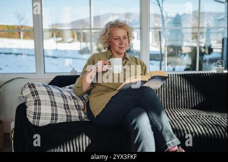 Senior woman drinking coffee and reading a book at home. Stock Photo