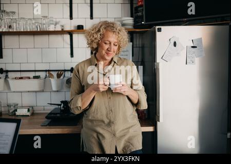 Happy middle-aged woman drinking coffee in the kitchen. Stock Photo