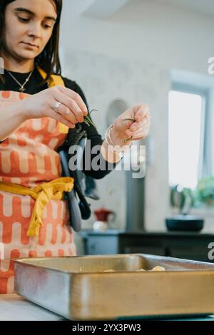 A woman is cooking in a kitchen with a pan on the stove. She is wearing an apron and has a ring on her finger Stock Photo