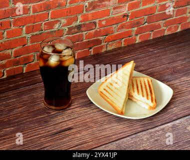 Two fresh sandwiches with meat and vegetables on a white ceramic plate and a tall glass of cola with ice on a wooden table. Close-up. Stock Photo