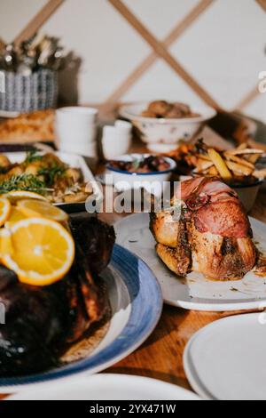 A table full of food, including a large piece of meat, a plate of chicken, and a plate of oranges Stock Photo