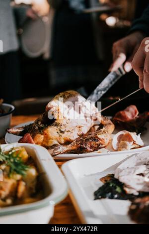 A person is cutting a piece of meat on a plate. The plate is on a table with other plates of food. Scene is casual and relaxed, as it is a family meal Stock Photo