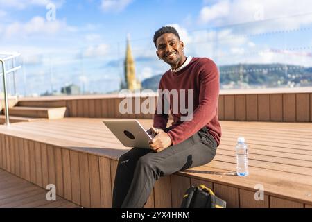 African man using laptop sitting on a terrace with views of a modern city Stock Photo