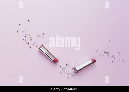 Two pink lipsticks with crushed glass pieces pink background Stock Photo