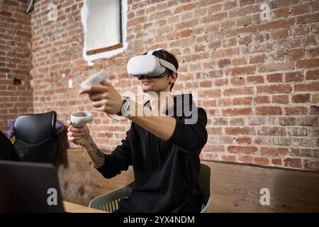 A man fully engaged in virtual reality, using a VR headset and controllers, exploring a digital world, technology engagement concept Stock Photo
