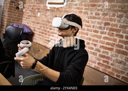 Young man exploring virtual reality gaming experience while using VR headset and controllers in an indoor modern setting technology concept Stock Photo
