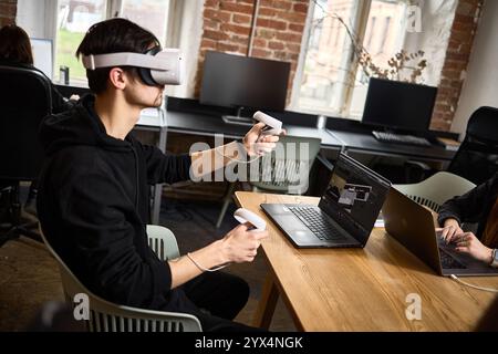 In a modern office, a man uses a virtual reality headset with controllers, showcasing technology and innovation in the work environment concept Stock Photo