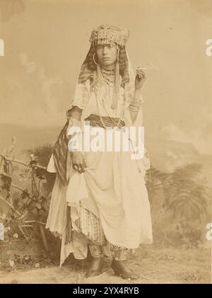 Woman smoking, about 1865-1885.  Additional Info: Studio portrait of a woman standing and smoking a cigarette. The woman has her hair braided into two loops, tucked underneath a round hat with small tassles. She is wearing large hoop earings with long chains hanging from each hoop. The woman is in a light colored dress with a dark sash. Stock Photo