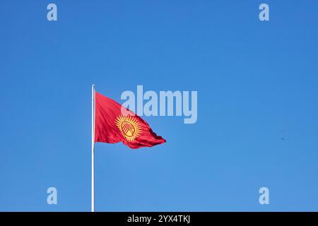 The main symbol of the Kyrgyz Republic. A red flag with a yellow sun fluttering in the wind, real photo. Ala-Too Square, Bishkek, Kyrgyzstan. Stock Photo